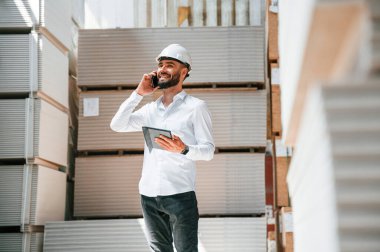 Telefonla konuşuyorlar. Depo işçisi depoda bir sürü ürünle birlikte..