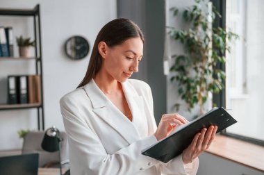 Not defterinde belge okunuyor. Resmi giyinmiş güzel bir kadın ofiste çalışıyor..