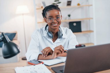 Masada dizüstü bilgisayarla. Beyaz gömlekli Afro-Amerikan kadın evde..