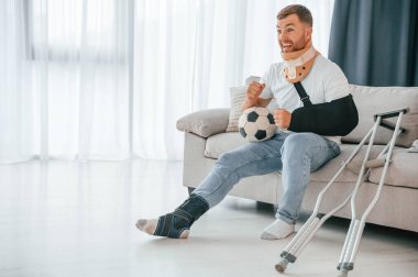 Oturmak, futbol topu tutmak, maç izlemek. Koltuk değnekli adam evde. Yaralı..