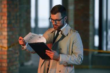 Ceketli erkek dedektif inşaat alanındaki bir suç mahallinde kanıt topluyor..