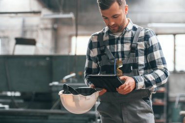 Siyah renkli tablet ellerinde. Üniformalı fabrika çalışanı içeride..