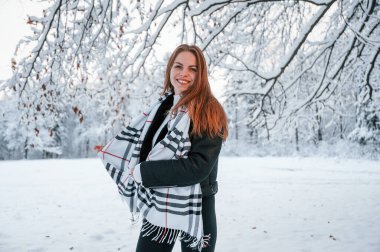 Ayakta durup eğlenmek. Sıcak bir eşarpla. Güzel genç bir kadın kış ormanında dışarıda..