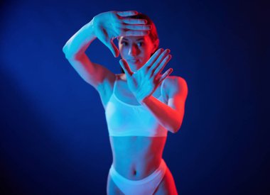 Elleriyle jestler yapıyor. İç çamaşırlı genç kadın stüdyoda neon ışıklarıyla bekliyor..