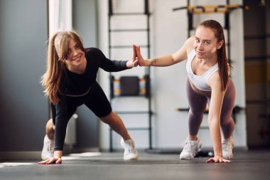 Şınav çekip çak bir beşlik. Spor elbiseli iki kadın spor salonunda birlikte spor yapıyorlar..