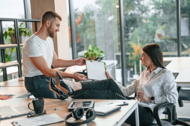 Sakin ol, bacaklar masanın üstünde. Erkek ve kadın modern ofiste birlikte çalışıyorlar..