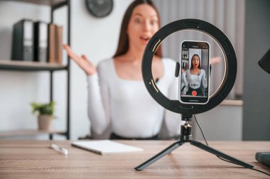 Kürsüdeki akıllı telefon kayıt yapıyor. Çevrimiçi ana sınıf. Beyaz elbiseli genç ve güzel bayan ofiste..