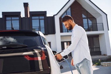 Aracı şarj etme işlemi. Genç şık adam, gündüz vakti elektrikli arabayla geziyor..