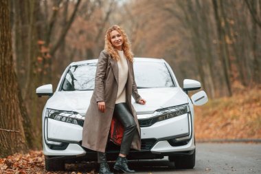 Kadın dışarıda, yolda elektrikli arabasının yanında duruyor..