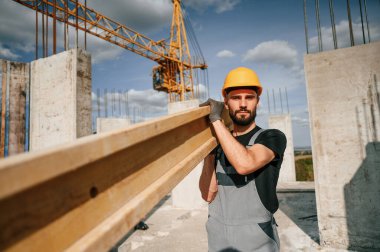 Tahta tahta ellerde. Üniformalı adam inşaat alanında çalışıyor..