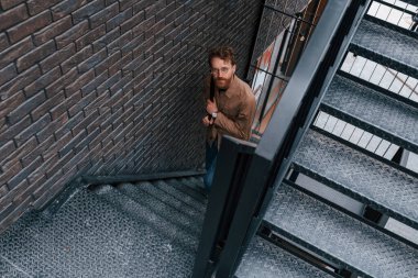 Yukarı bakıyorum. Haki renkli ceketli ve kot pantolonlu adam binanın merdivenlerinde açık havada..