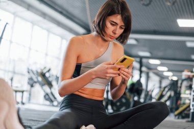 Akıllı telefon kullanıyor. İnce vücutlu spor elbiseli kadın spor salonunda..