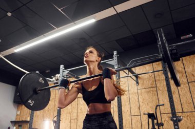 Çömeliyor. Kadın spor salonunda halter kaldırıyor..