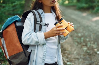 Sarı renkli dürbünle. Kız yaz günü ormanda yeni yerler keşfediyor..