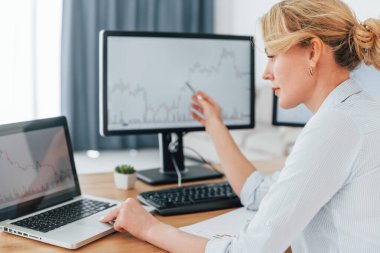 Grafikteki işareti göstermek için kalem kullanılıyor. Resmi giyimli kadın borsacı ofiste çalışıyor..