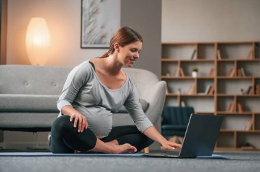 Laptop kullanarak yoga dersleri alıyorum. Güzel hamile kadın evde..