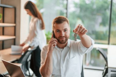 Yeni dairenin anahtarlarını saklıyorum. Erkek ve kadın modern ofiste birlikte çalışıyorlar..