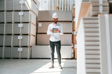 Resmi kıyafetler içinde ciddi bir yönetici. Depo işçisi depoda bir sürü ürünle birlikte..