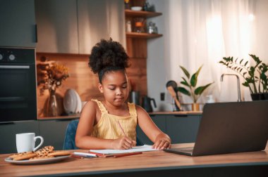Çizim yapmak için dizüstü bilgisayar ve kağıtla masada oturuyordum. Gündüz vakti evde rahat giyinen sevimli siyah kız var..