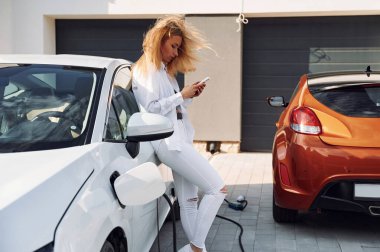 Şarj işlemi. Beyaz elbiseli genç bir kadın gündüz vakti elektrikli arabasıyla geliyor..