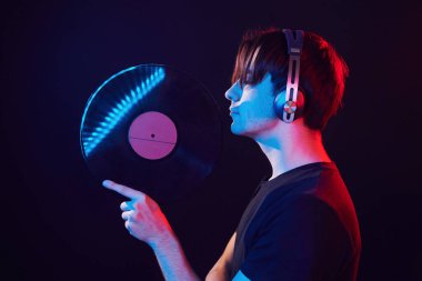 With vinyl record in hands. Man standing in the studio with neon light.