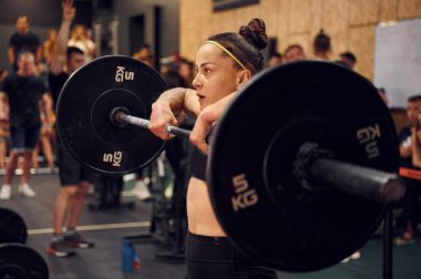 Çömeliyor. Kadın spor salonunda halter kaldırıyor..