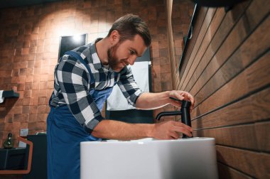 Lavabo ve musluğu tamir ediyorum. Mavi üniformalı tesisatçı banyoda çalışıyor..