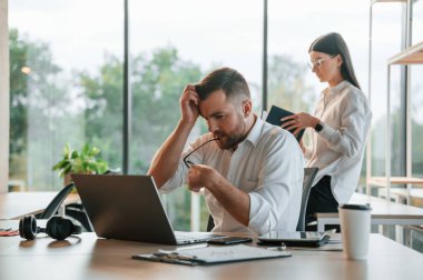 Masanın yanında oturan beyaz kadın arka planda. Çalışanlar modern ofiste birlikte çalışıyorlar..