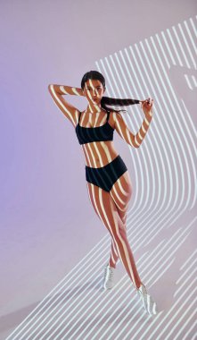 Siyah iç çamaşırlı esmer ayakta duruyor ve poz veriyor. Stüdyoda projektör neon ışıkları altında güzel genç bir kadın var..