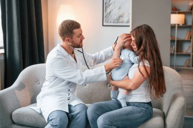 Steteskop kullanıyorum. Erkek doktor, kadının yeni doğan bebeğine evde bakıyor..