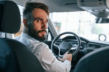 Arkana bak. Beyaz elbiseli genç adam araba galerisinde..