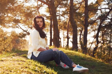 Güzel bir kadın gündüz vakti ormanda çimlerin üzerinde oturuyor..