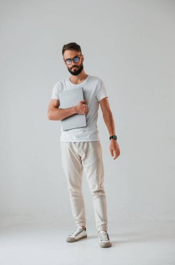 Gümüş renkli dizüstü bilgisayar ellerinde. Yakışıklı adam stüdyoda beyaz arka plana karşı..