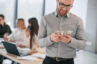 Adam parayı elinde tutuyor. Ofiste başarılı bir ekip birlikte çalışıyor. İş kavramı.