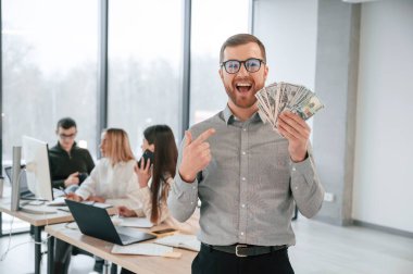 Adam parayı elinde tutuyor. Ofiste başarılı bir ekip birlikte çalışıyor. İş kavramı.