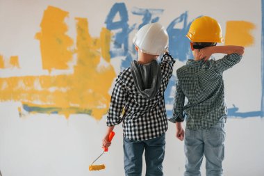 Sert şapkalarla. İki çocuk ev odasında duvar boyuyor..