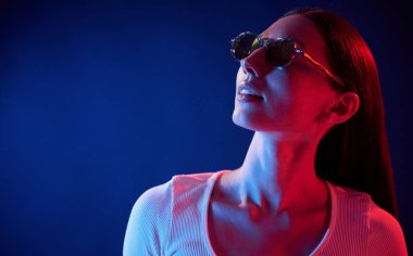 Durup poz vermek. İçerideki neon ışıkta duran genç bir kadının portresi..