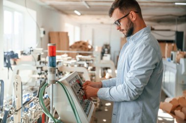 Makine operatörü bir cihaz kurmakla meşgul. Beyaz elbiseli matbaacı içeride..