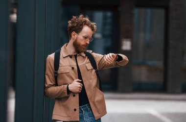 Saatlere bakıyorum. Sakallı, haki renkli ceketli ve kot pantolonlu şık bir adam binanın yanında..