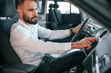 Yan görüş. Bir otomobilin içinde oturuyor. Beyaz elbiseli genç adam araba galerisinde..