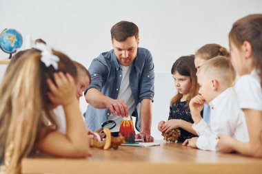 Küçük volkan modeline bakıyorum. Okulda öğretmenle birlikte bir grup çocuk öğrenci..