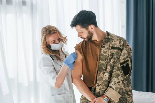 stock image Soldier get vaccinated by female doctor indoors.