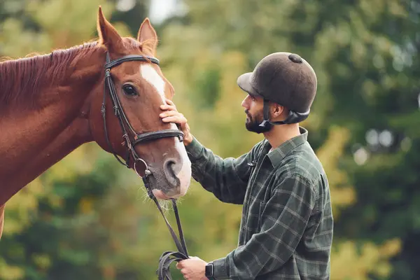 stock image In protective hat. Young man with a horse is outdoors.