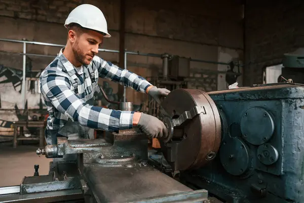 Üniformalı fabrika çalışanı içeride. Metal üzerinde işlem yapılıyor..