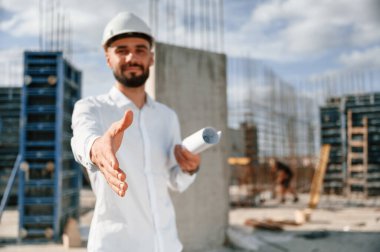 Mühendis elini uzatıyor. Üniformalı adam inşaat alanında çalışıyor..