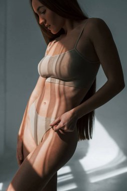 Pencerelerden güneş ışığı geliyor. Stüdyoda zayıf vücutlu bir kadın poz veriyor..