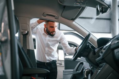 Otomobilin salonunu inceliyorum. Beyaz elbiseli genç adam araba galerisinde..