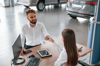 Masanın başında oturup anahtarları almak. Beyaz elbiseli bir adam araba galerisinde birlikte..