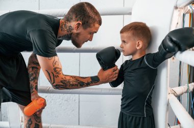 Beginning of the professional sport. Coach is teaching the boy box techniques indoors. clipart