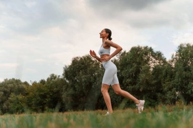Koşu, günlük spor rutini. İnce vücutlu beyaz bir kadın açık havada spor kıyafetleri giyiyor..